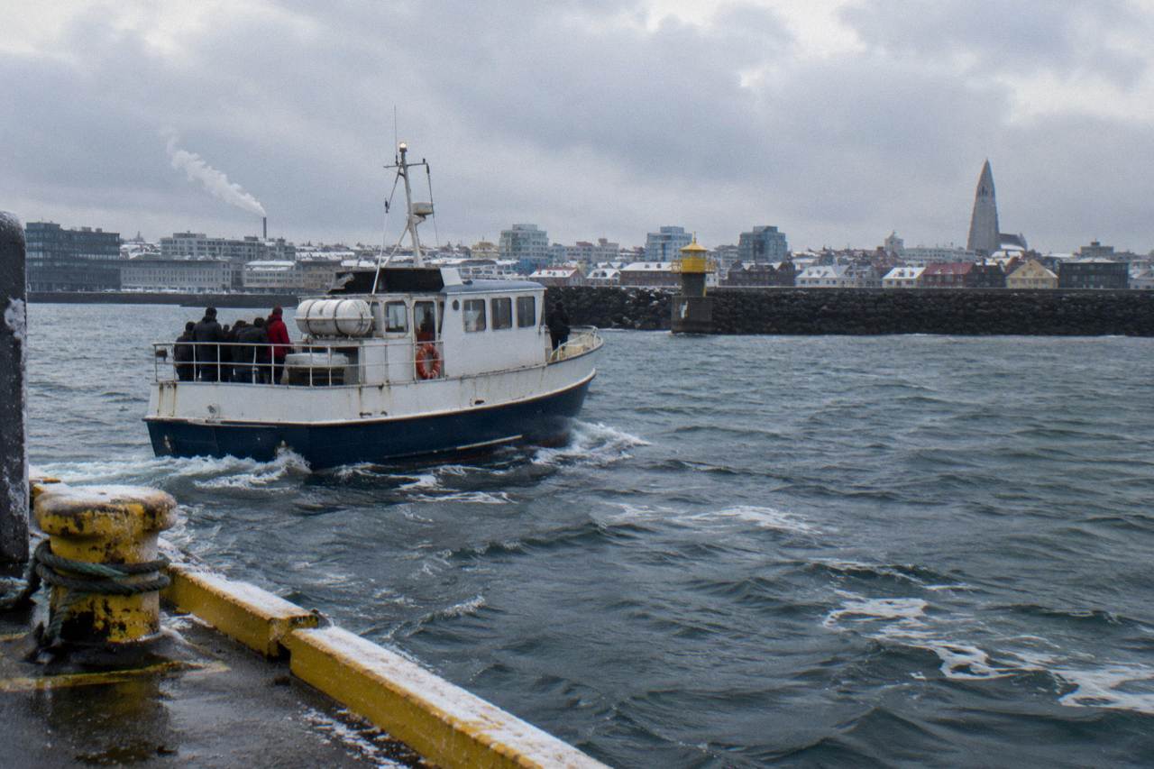 A small whale watching boat leaving Reykjavik Old Harbour under a low winter sky