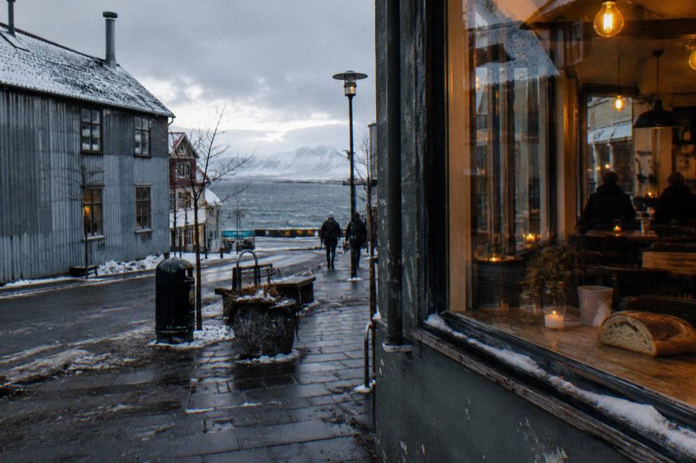 A restaurant window glowing warmly against a dark winter street with snow dusting