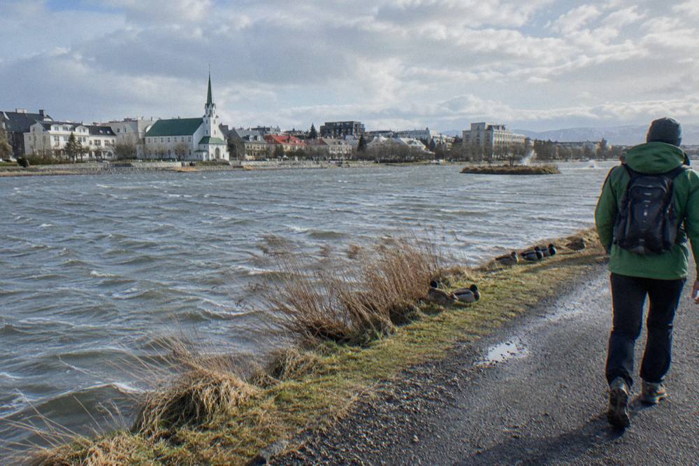 A walker in a layered outfit with rain shell on a Reykjavik sidewalk