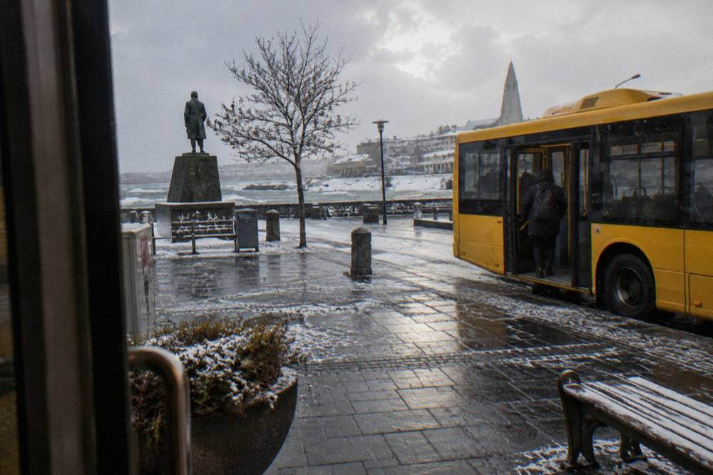 City bus parked at a stop on a wide Reykjavik street under a grey sky